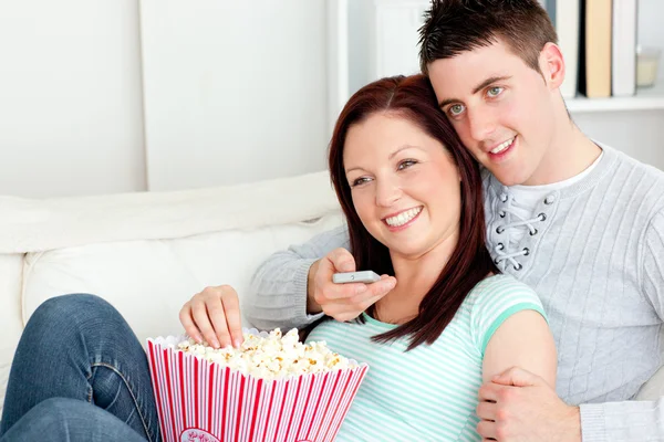 Affectionate couple lying on the sofa watching television in the — Stock Photo, Image