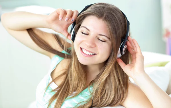 高兴听音乐用耳机在沙发上的女人 — 图库照片