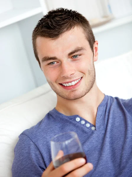 Όμορφος νέος άνθρωπος που κρατά ένα ποτήρι κρασί, καθμένος σε έναν καναπέ σε — Φωτογραφία Αρχείου
