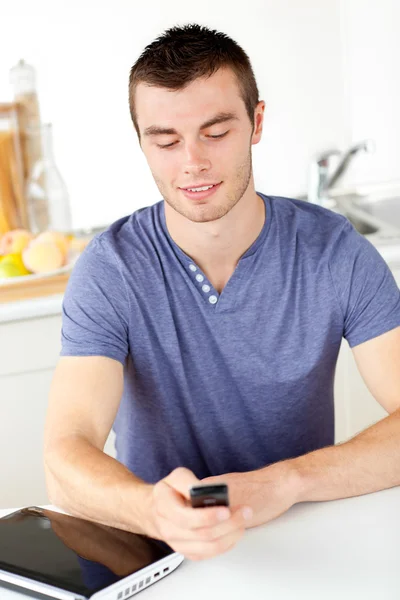 Positive young man sending a text in the living-room — Stockfoto