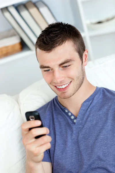 Uroczy młody człowiek wysyła tekst i uśmiechając się w pokoju dziennym — Zdjęcie stockowe