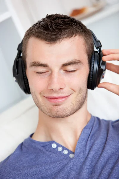 Lively young man listening to music sitting on the couch in the — Stock Photo, Image