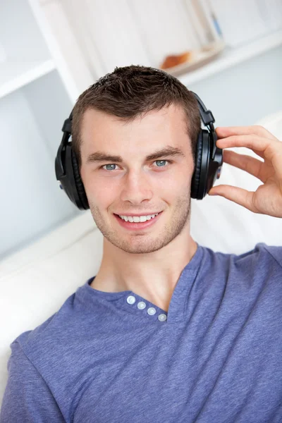 Bright young man listening to music sitting on the couch in the — Stock Photo, Image