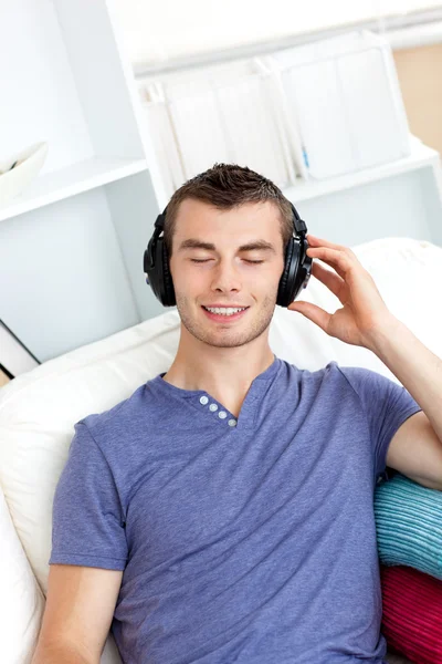 Spokojny młody człowiek, słuchanie muzyki, siedząc na kanapie w — Zdjęcie stockowe