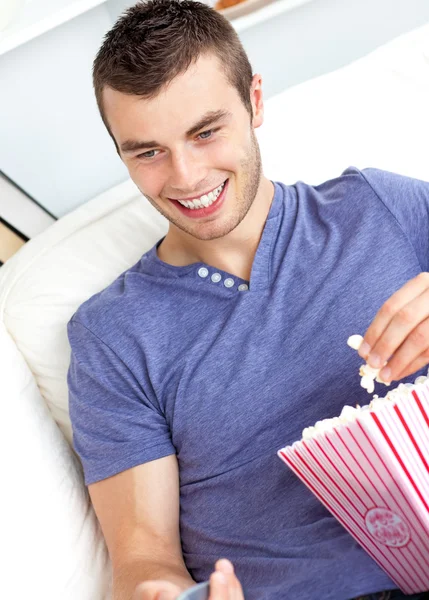 Positivo uomo caucasico in possesso di un telecomando e mangiare popcorn in th — Foto Stock