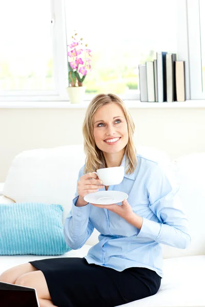 Улыбающаяся деловая женщина, держащая чашку кофе сидя на диване — стоковое фото