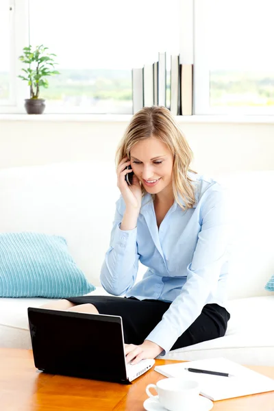 Drukke zakenvrouw met behulp van haar laptop en haar mobiele telefoon thuis — Stockfoto
