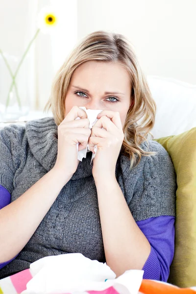 Sick woman using a tissue sitting on a sofa — Stock Photo, Image