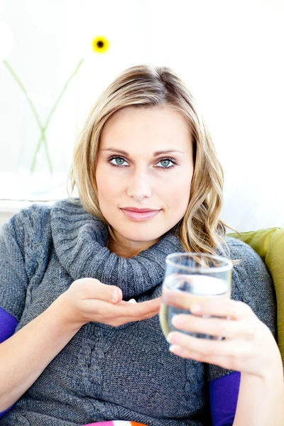 Mujer enferma tomando píldoras sosteniendo un vaso de agua sentado en un tan —  Fotos de Stock
