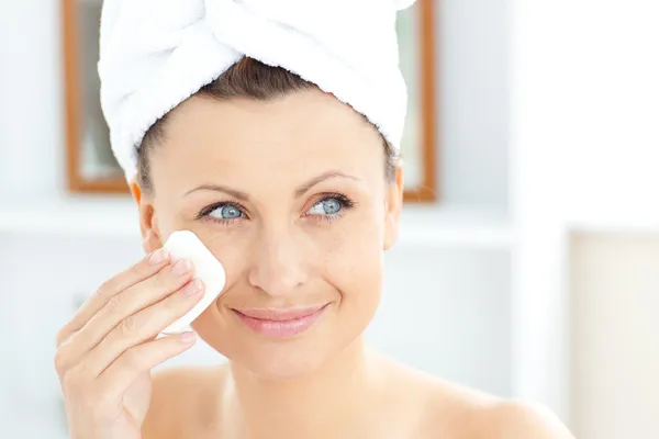 Jonge vrouw zetten crème op haar gezicht dragen een handdoek in de vleermuis — Stockfoto