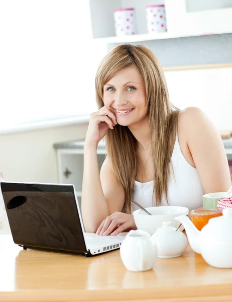 Leende kvinna att ha frukost och använda sin bärbara dator ser på t — Stockfoto