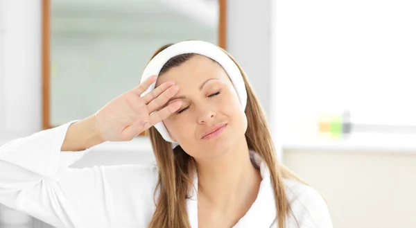 Positieve vrouw zetten crème op haar gezicht dragen een hoofdband in t — Stockfoto