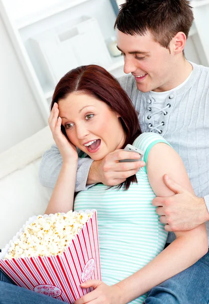 Jeune couple couché sur le canapé avec popcorn et télécommande — Photo