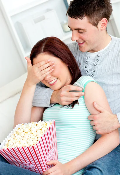 Charming couple lying on the sofa with popcorn and remote — Stock Photo, Image
