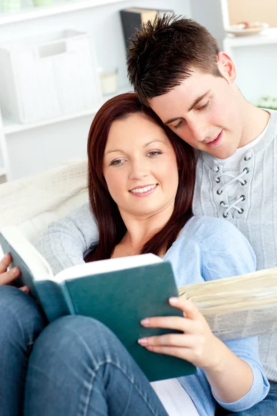 Coppia felice che legge un libro nel salotto sdraiato sul divano — Foto Stock