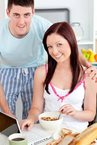 Χαμογελώντας ζευγάρι χρησιμοποιώντας ένα φορητό υπολογιστή ενώ το πρωινό στο σπίτι — Φωτογραφία Αρχείου