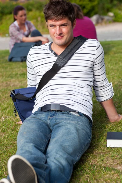 Hombre guapo estudiante acostado en la hierba con su mochila — Foto de Stock