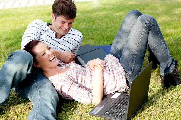 Couple of bright students using a laptop lying on the grass — Stock Photo, Image