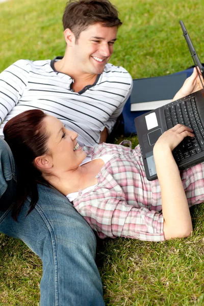 Un paio di studenti positivi utilizzando un computer portatile sdraiato sull'erba — Foto Stock