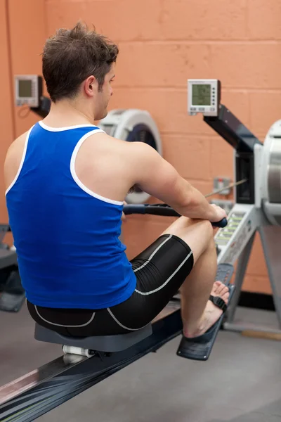 Athletic caucasian man using a rower — Stock Photo, Image