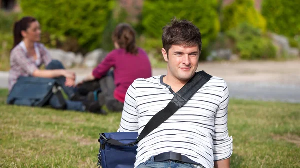Положительный студент-мужчина лежит на траве со своей школьной сумкой — стоковое фото