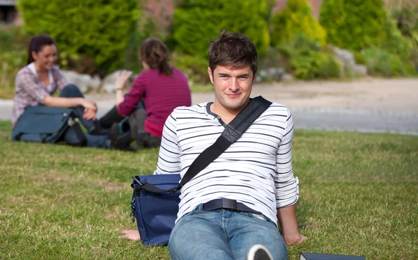 Estudante do sexo masculino bem parecido deitado na grama com sua mochila escolar — Fotografia de Stock