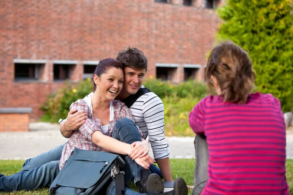 Happy couple of students sitting on grass talking with a female — Stock Photo, Image