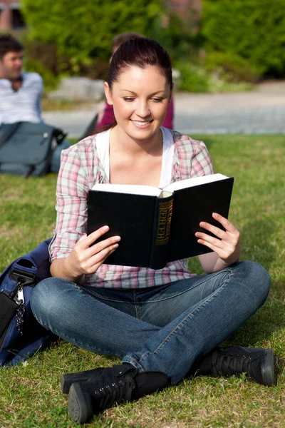 Young female student reading a book sitting on grass — Stock Photo, Image