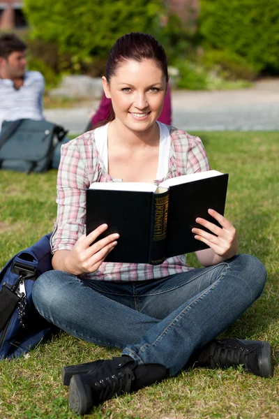 Estudiante seria leyendo un libro sentado en la hierba — Foto de Stock