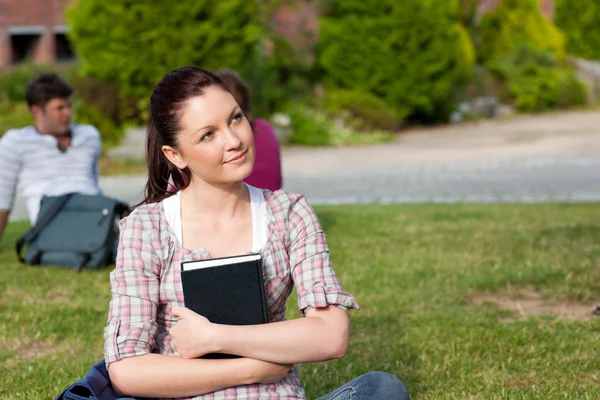 Thoughtful female student reading a book sitting on grass — Stock Photo, Image