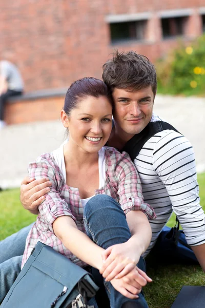Belo casal de estudantes sentados na grama e sorrindo para o — Fotografia de Stock