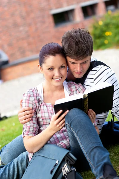 Молодая пара студентов читает книгу, сидя на траве — стоковое фото