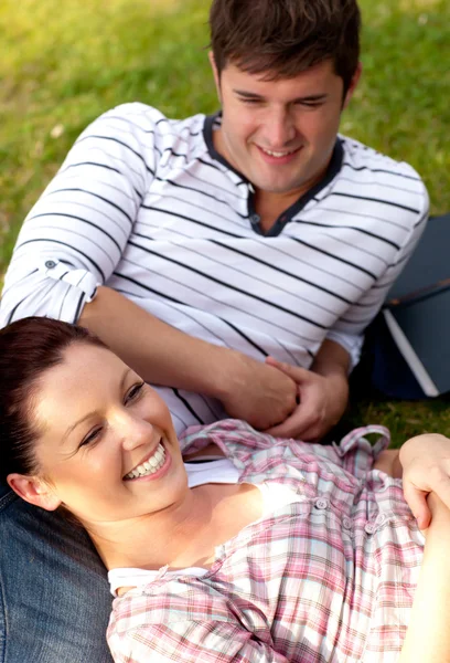 Casal positivo de estudantes sentados na grama e sorrindo para o — Fotografia de Stock