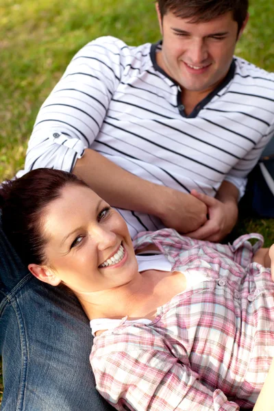 Joyful couple of students sitting on grass and smiling at the ca — Stock Photo, Image