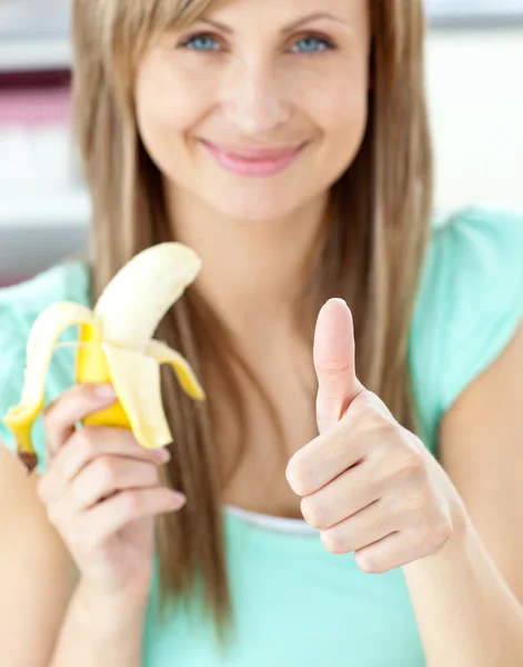 Χαμογελαστή γυναίκα με τον αντίχειρα επάνω κρατώντας μια μπανάνα στην κουζίνα — Φωτογραφία Αρχείου