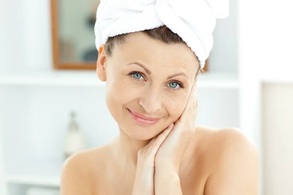 Attraente giovane donna con un asciugamano mettendo crema sul viso in — Foto Stock
