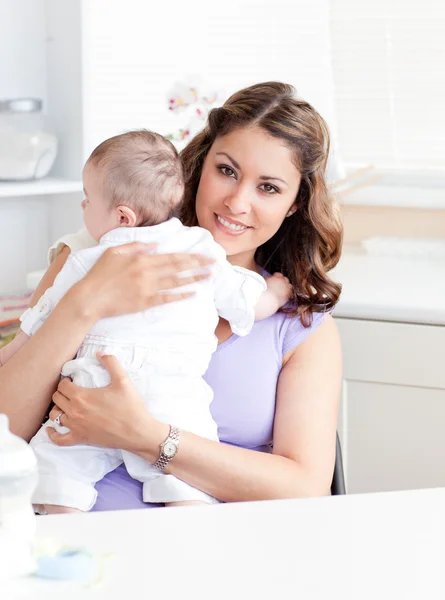 Позитивная молодая мать держит своего ребенка на кухне — стоковое фото