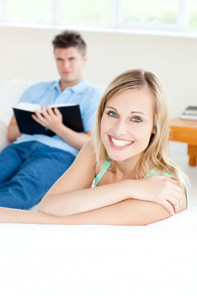 Fidanzata sorridente alla fotocamera mentre il suo fidanzato sta leggendo — Foto Stock