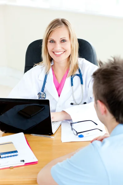 Lächelnde Ärztin, die ihren Laptop benutzt und mit ihrem männlichen Kollegen spricht — Stockfoto