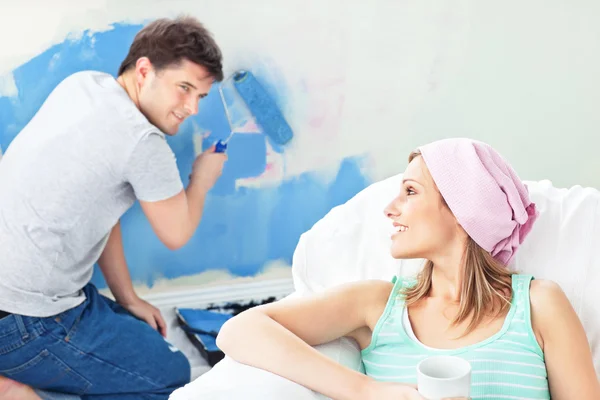 Vacker kvinna avkopplande på en soffa medan pojkvän målning roo — Stockfoto