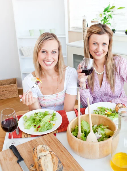 Mujeres guapas comiendo una ensalada y bebiendo vino en la cocina —  Fotos de Stock