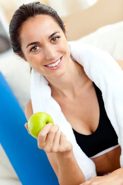 Mujer radiante comiendo una manzana en el sofá después de hacer ejercicio en t — Foto de Stock