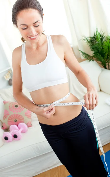 Jovem mulher positiva medindo sua cintura com uma fita em seu livi — Fotografia de Stock