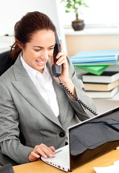 Ocupada mujer de negocios hablando por teléfono y usando su portátil sentado —  Fotos de Stock