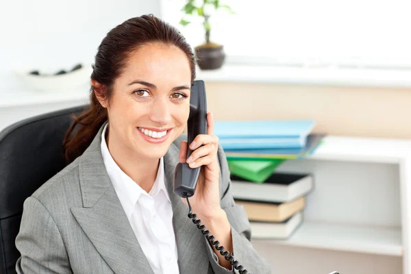 Positive businesswoman talking on phone sitting in her office — Stock Photo, Image