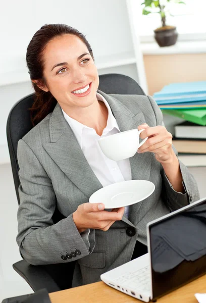 Mujer de negocios sosteniendo una taza de café delante de su computadora portátil sentarse — Foto de Stock