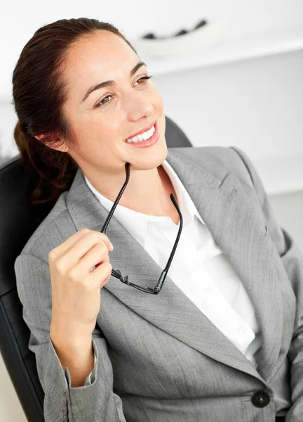 Assertive businesswoman holding her glasses sitting in her offic — Stock Photo, Image