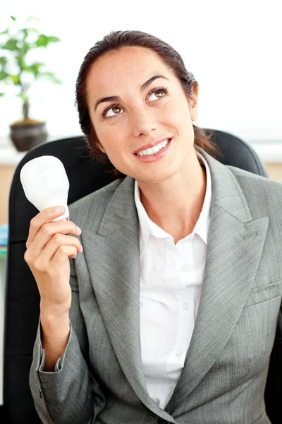 Empresária atenciosa segurando uma lâmpada na mão sentada — Fotografia de Stock