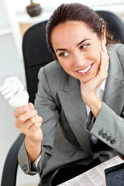 Pensativa mujer de negocios sosteniendo una bombilla sentada en su off — Foto de Stock