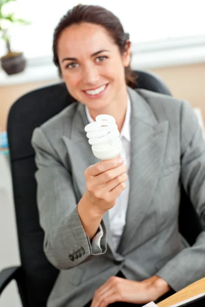 Empresária atraente segurando uma lâmpada sentada em seu off — Fotografia de Stock